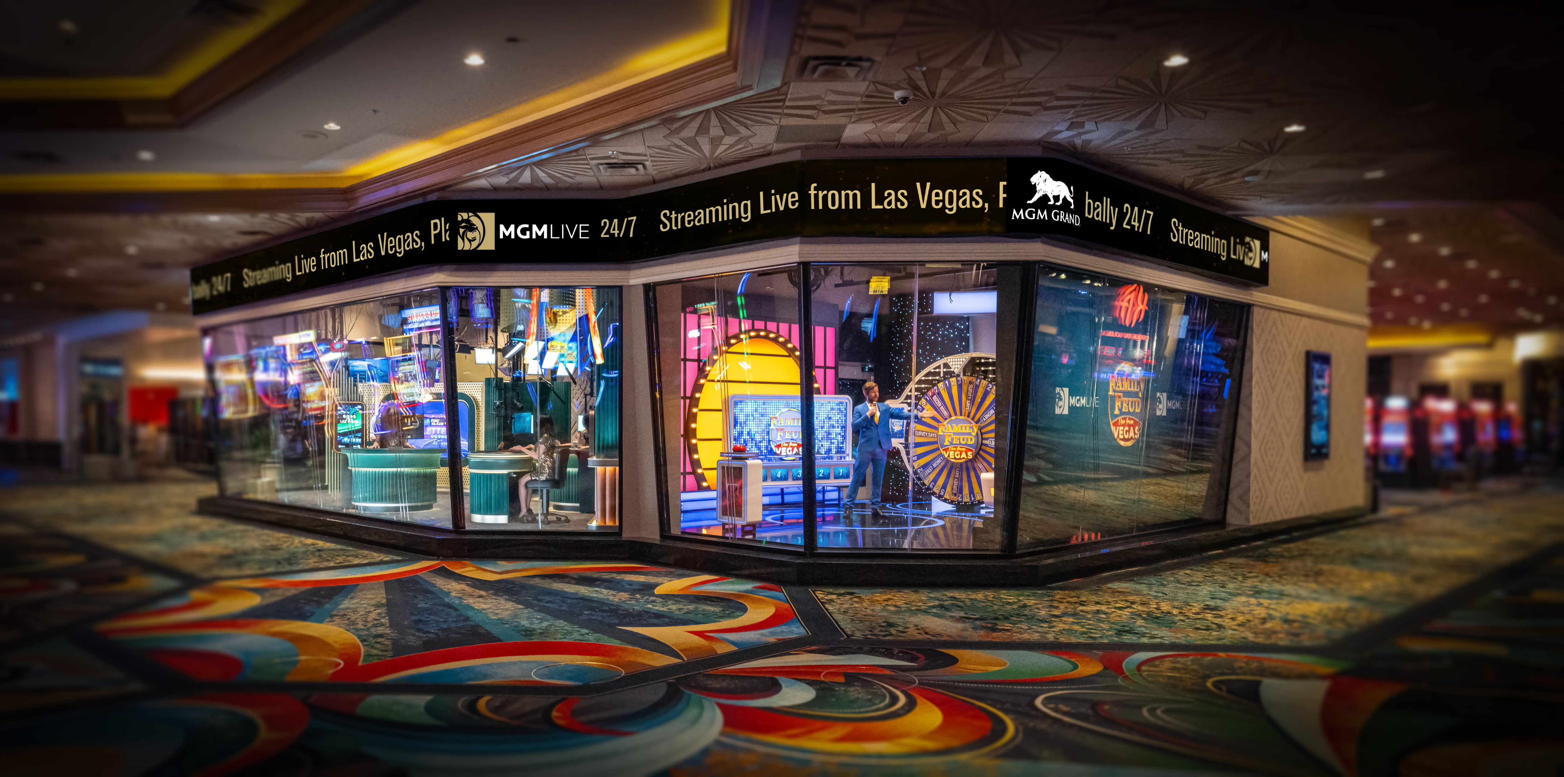 A futuristic glass studio on the MGM Grand casino floor with bright Vegas lights, showcasing a Family Feud-style game show in progress.