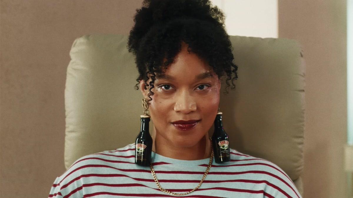 Woman in a hair salon wearing miniature Baileys Original Irish Cream bottles as earrings in the Bring on the Baileys holiday campaign